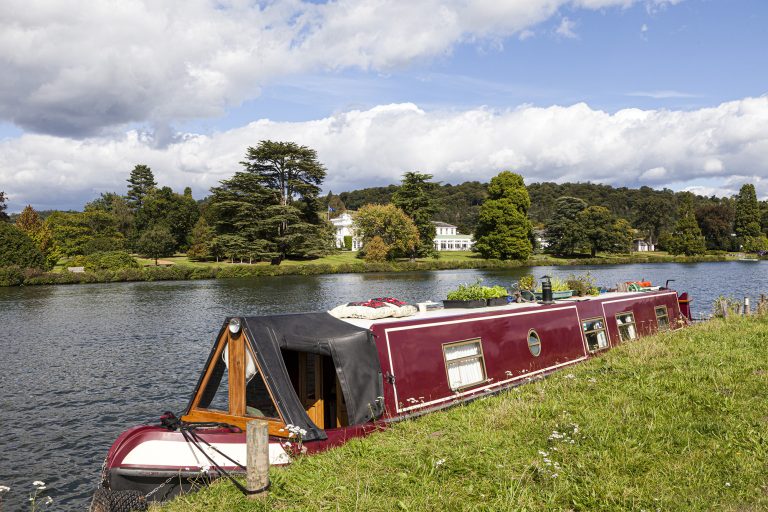 A narrow boat moored opposite Greenlands on the River Thames at Hambleden, Buckinghamshire, UK